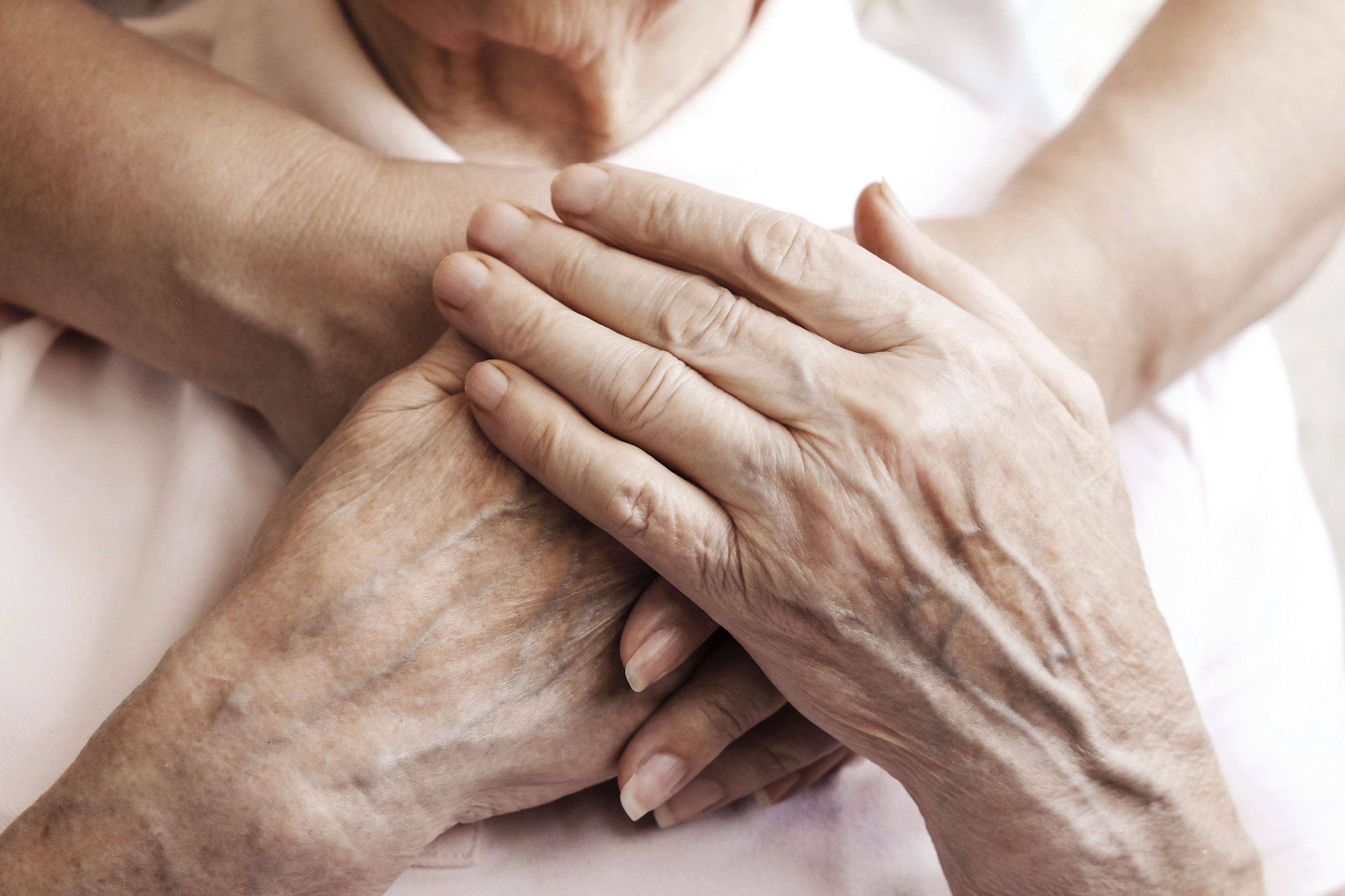 Mature female in elderly care facility gets help from hospital personnel nurse. Senior woman, aged wrinkled skin & hands of her care giver. Grand mother everyday life. Background, copy space, close up